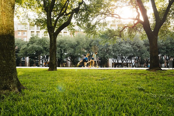 Distant Caucasian girls riding scooter in park