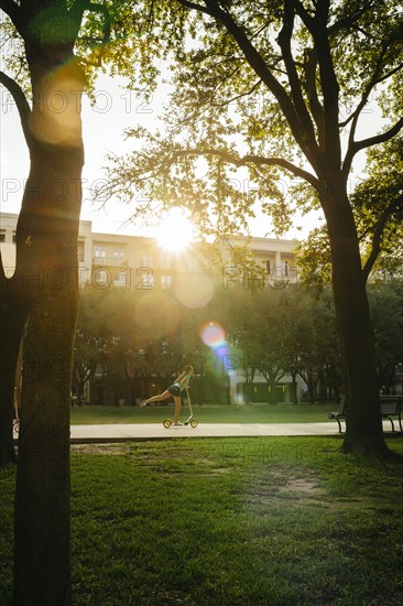 Distant Caucasian girl riding scooter in park