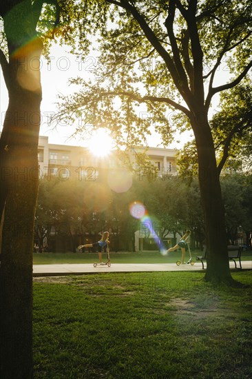 Distant Caucasian girls riding scooter in park