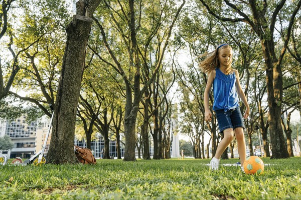 Caucasian girl kicking soccer ball in park
