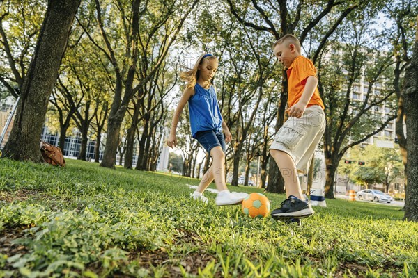 Caucasian brother and sister kicking soccer ball in park