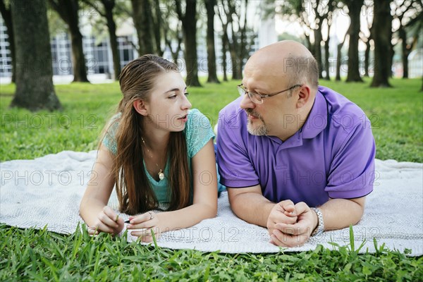 Serious Caucasian father and daughter talking on blanket in park