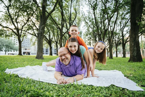 Portrait of Caucasian boy and girls laying on back of father in park