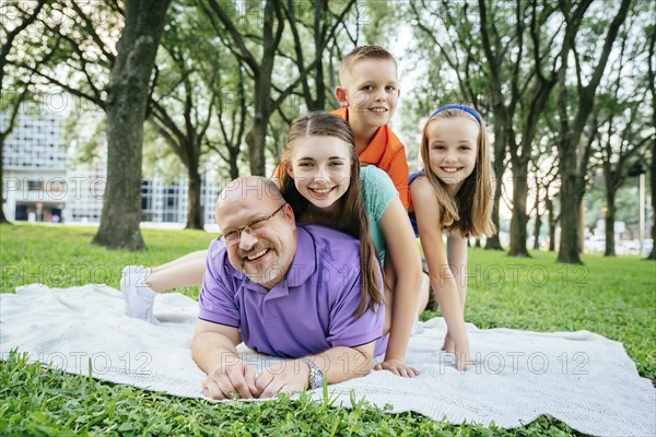 Portrait of Caucasian boy and girls laying on back of father in park