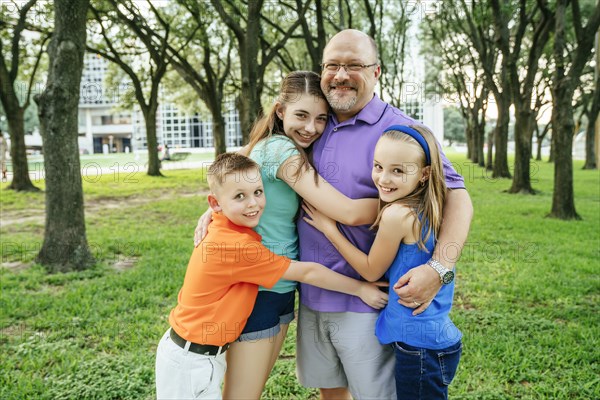 Portrait of Caucasian boy and girls hugging father in park