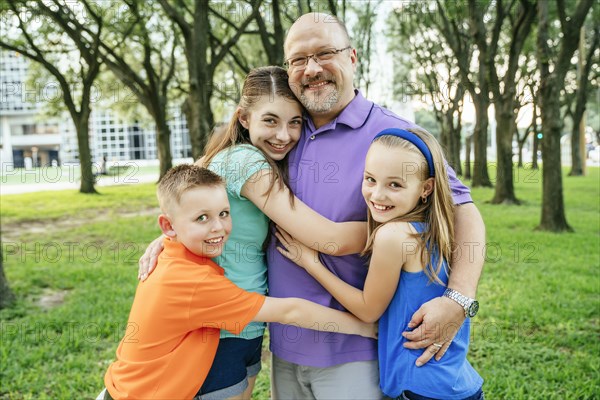 Portrait of Caucasian boy and girls hugging father in park