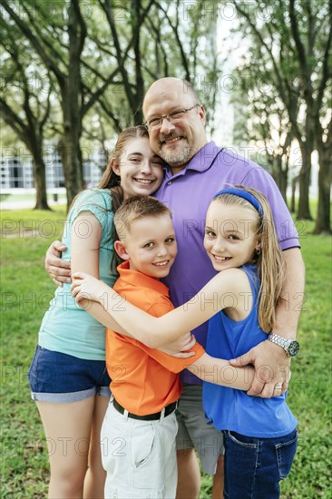 Portrait of Caucasian boy and girls hugging father in park