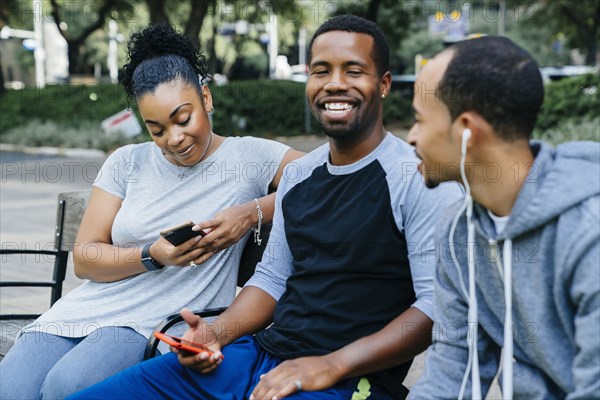 Black friends sitting on bench holding cell phones