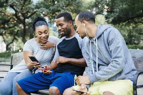 Black friends sitting on bench texting on cell phones