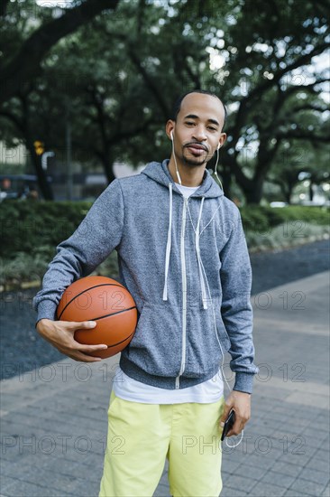 Portrait of Black man listening to earbuds and holding basketball