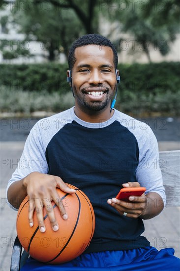 Portrait of Black man listening to earbuds and holding basketball