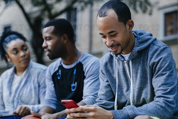 Black man texting on cell phone near friends