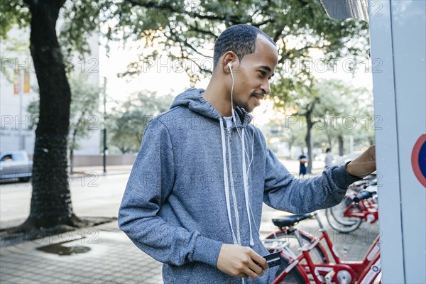 Black man with earbuds paying for bicycle rental with credit card