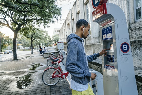 Black man with earbuds paying for bicycle rental with credit card