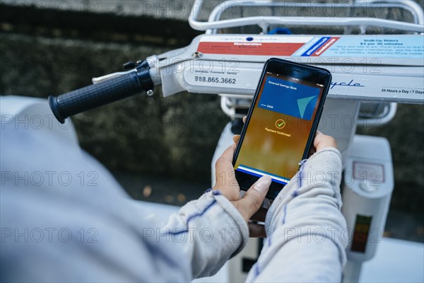 Hands of Black woman paying for bicycle rental with cell phone