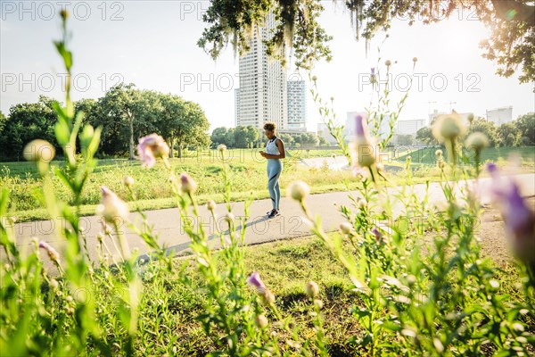 Mixed Race woman standing on running path in park beyond wildflowers