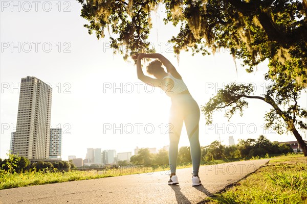 Mixed Race woman stretching on running path in park