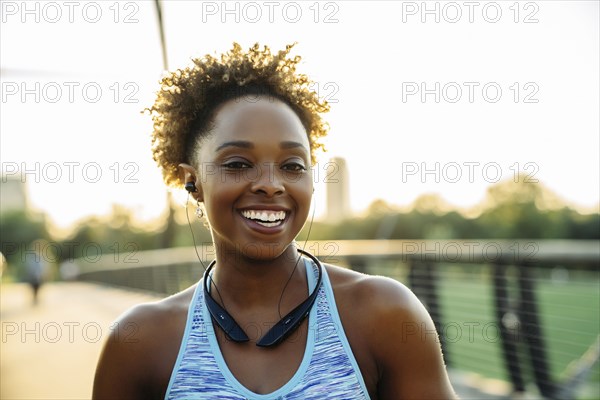 Smiling mixed race woman listening to earbuds on bridge