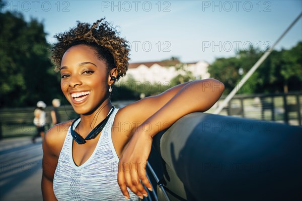 Smiling mixed race woman listening to earbuds on bridge