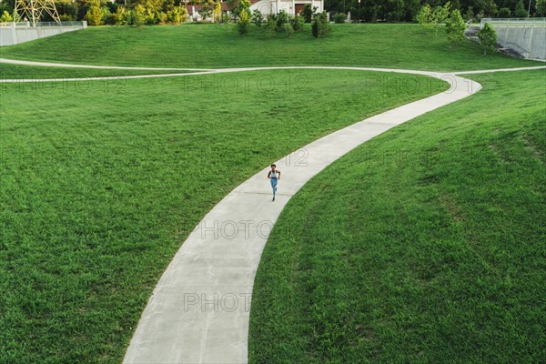 Distant mixed race woman running on winding path in park