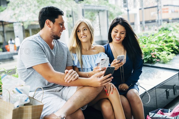 Friends sitting on bench texting on cell phones