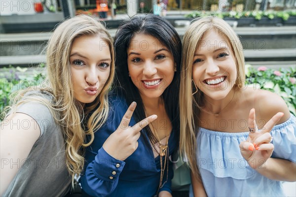 Smiling women posing and gesturing for cell phone selfie