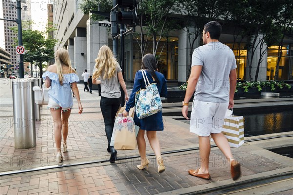 Friends crossing street in city carrying shopping bags