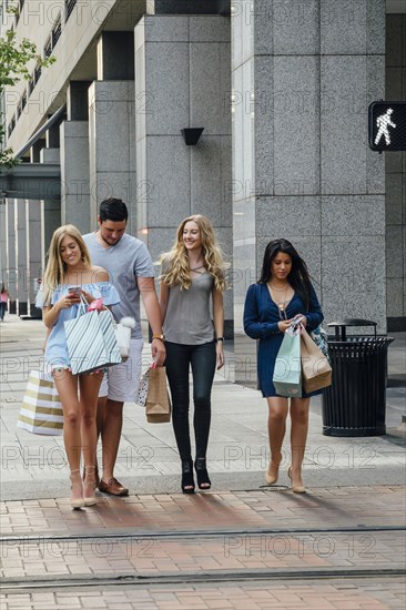 Friends walking in city carrying shopping bags texting on cell phones