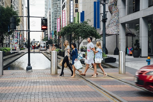 Friends crossing street in city carrying shopping bags