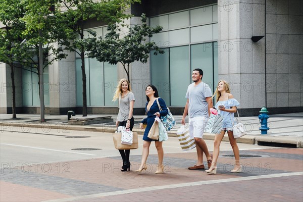 Friends crossing street in city carrying shopping bags