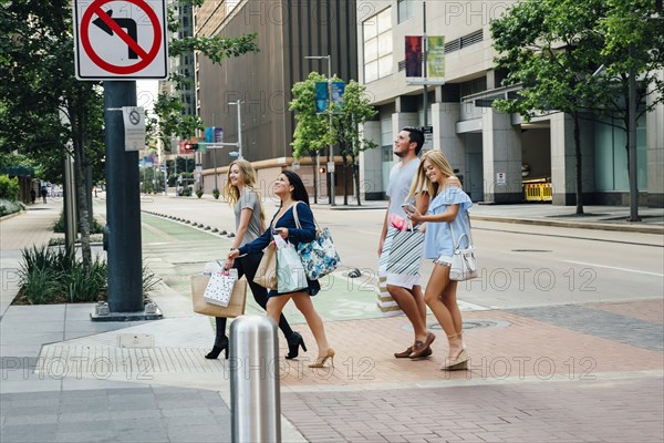 Friends crossing street in city carrying shopping bags