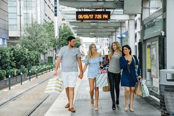 Friends walking at train station carrying shopping bags