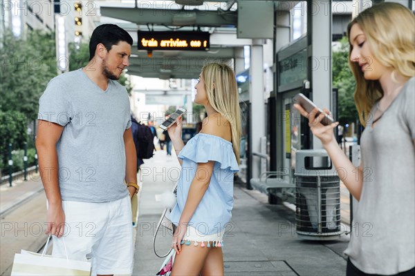 Caucasian woman showing cell phone to man at train station