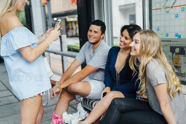 Woman photographing friends at train station with cell phone