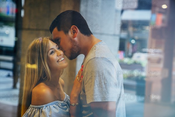 Caucasian man kissing woman on cheek behind window