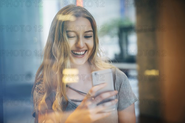 Smiling Caucasian woman posing for cell phone selfie behind window