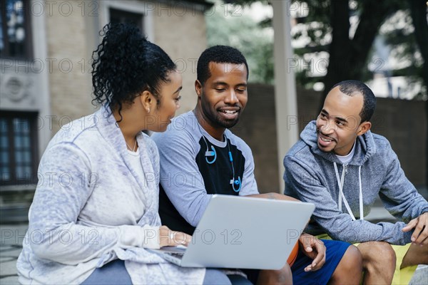 Black friends sitting outdoors using laptop