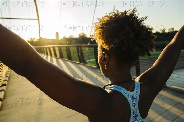 Mixed Race woman wearing earbuds stretching arms on bridge