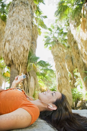 Hispanic woman listening to mp3 player in tropical area