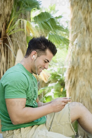 Hispanic man listening to mp3 player in tropical area