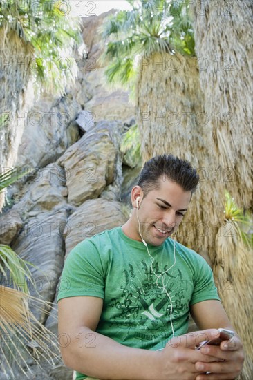 Hispanic man listening to mp3 player in tropical area