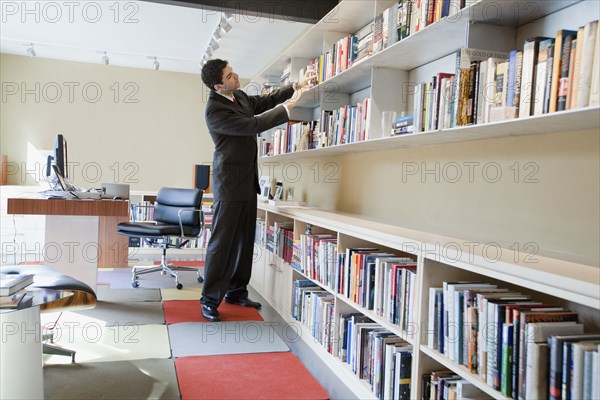Mixed race businessman taking book from shelf