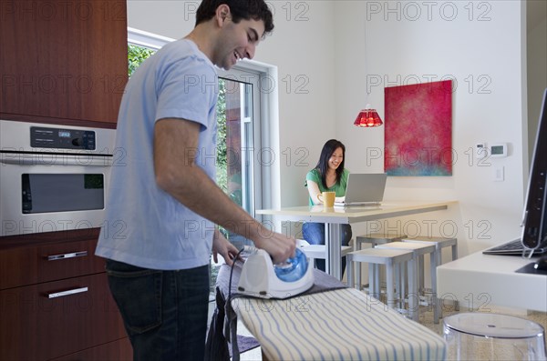 Husband ironing while wife uses laptop