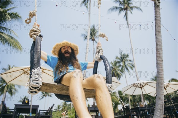 Caucasian man sitting on rope swing yelling