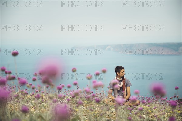 Caucasian man sitting in field of flowers near ocean