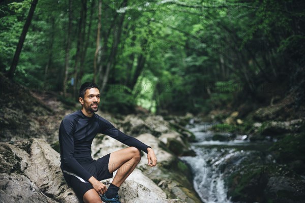 Caucasian man sitting on rocks near forest stream