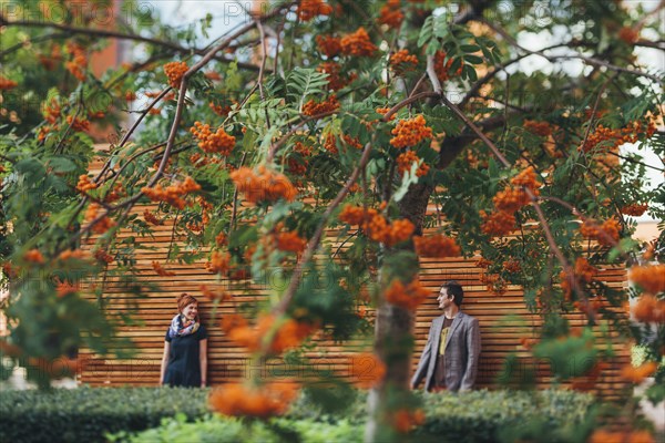 Smiling Caucasian couple leaning on wooden wall behind tree