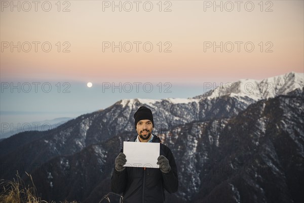 Smiling Caucasian man holding blank sign in mountain landscape