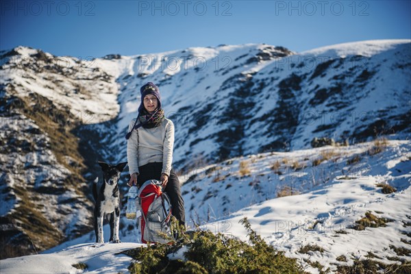 Caucasian woman posing with dog and backpack on mountain