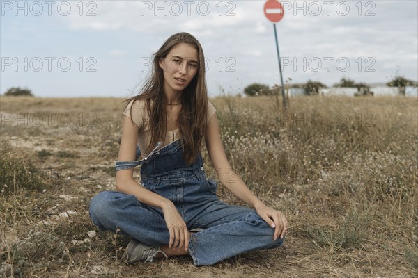 Caucasian woman wearing overalls sitting in rocky field